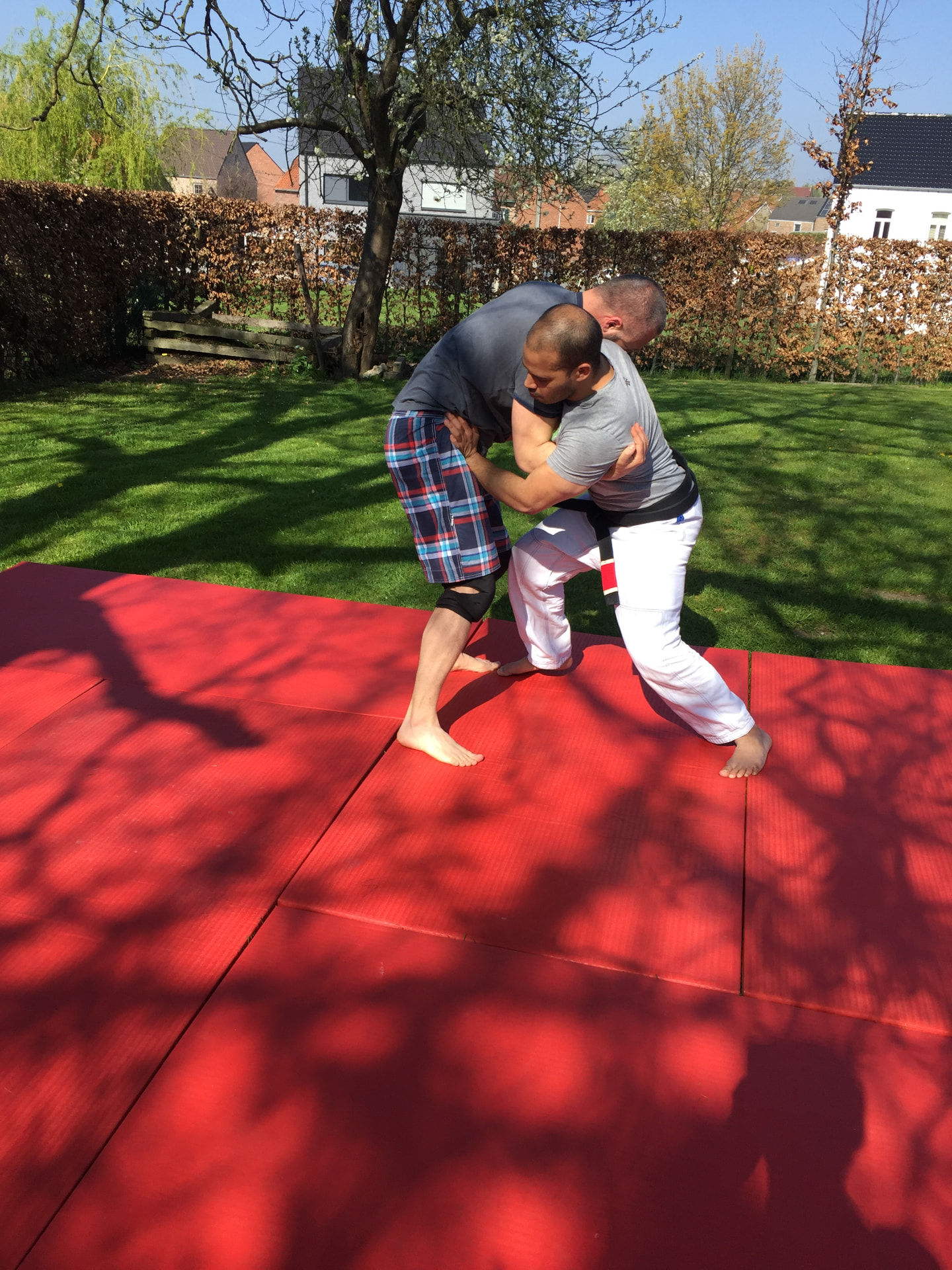 Outdoor jiu-jitsu training on a red mat in the garden